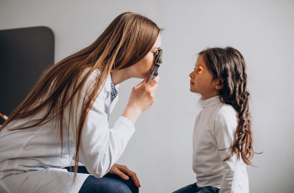 An optometrist examines a child's eyes with a handheld light during an eye exam.