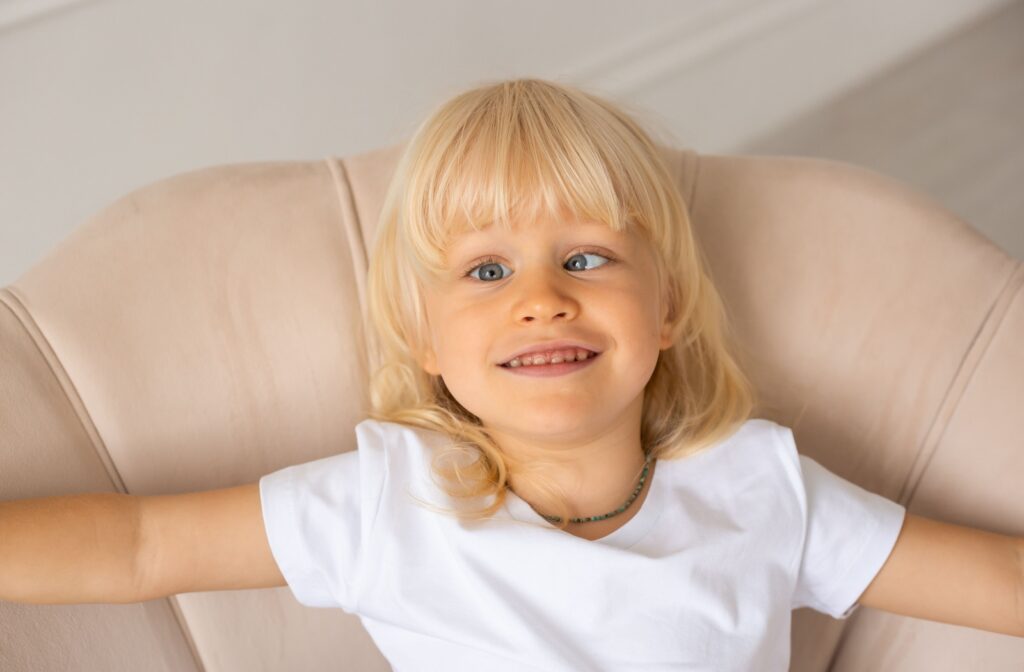A young child with crossed eyes sitting in a tan couch.
