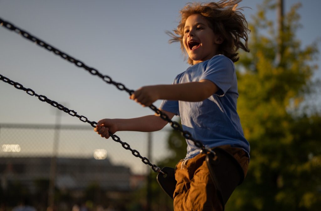 A child smiling as they swing on a swing outside not wearing glasses or contacts